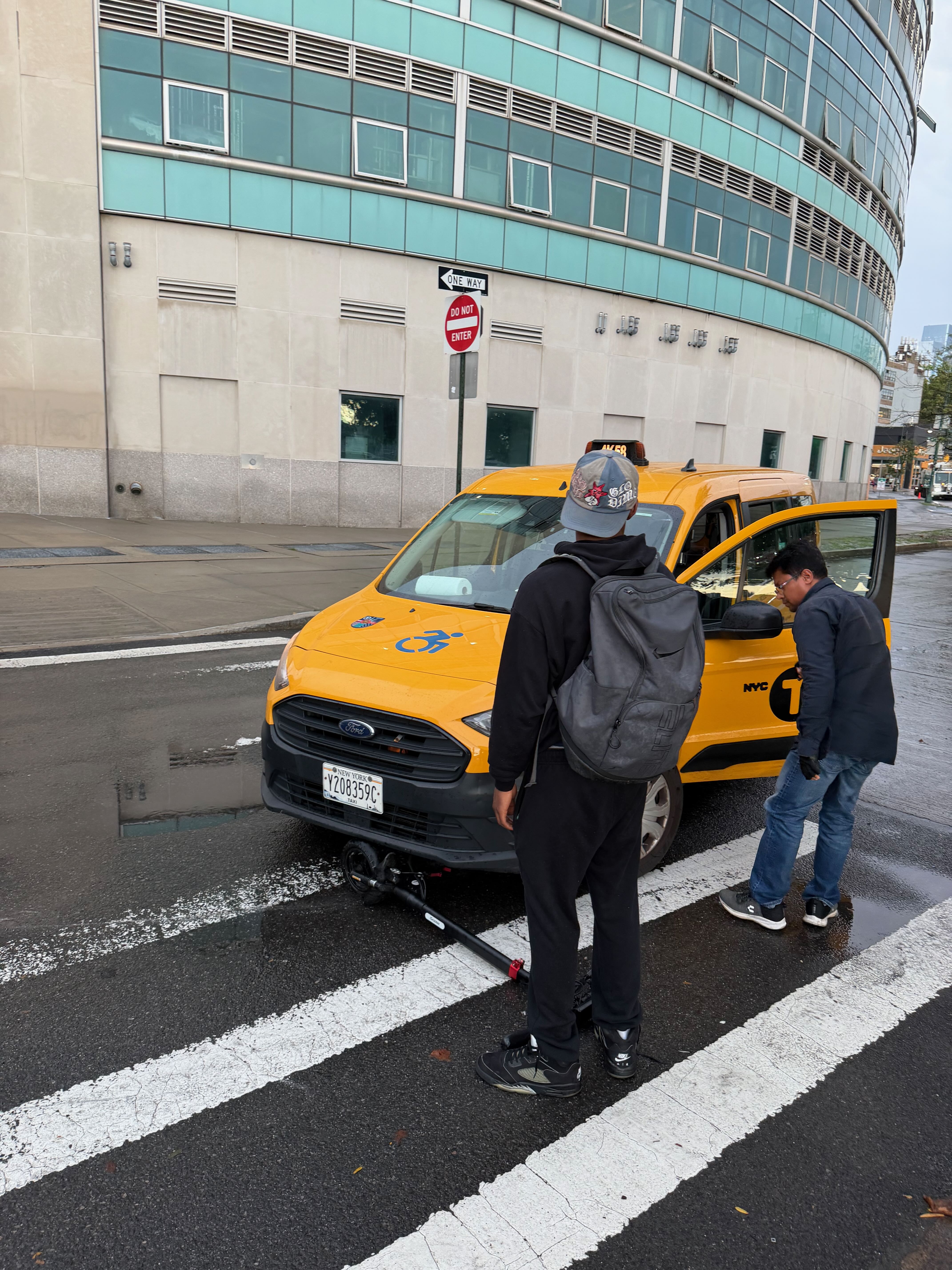 Kid trying to get his scooter out from under a taxi.